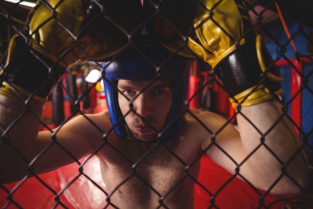 Boxer wearing headgear leaning against wire mesh fence
