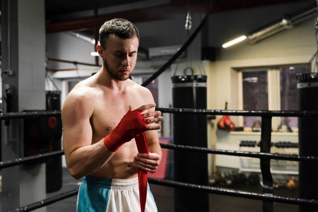Male boxer wrapping hand with red bandage in ring